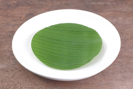 Ceramic plate with banana leaves in the plate on a wooden table, top view above.  Mockups can be used to edit food product displays or design layouts.の写真素材