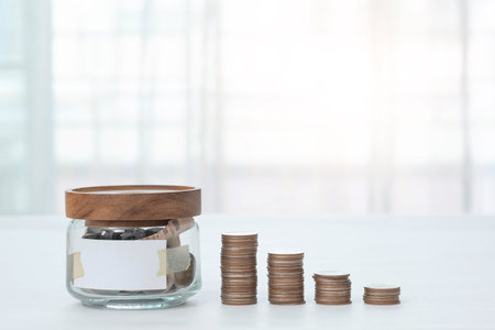 Jar with money inside with empty label and stacked coins with blurred background. Finance business concept.の写真素材
