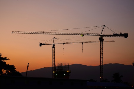 Industrial construction cranes and building silhouettes at sunset の写真素材