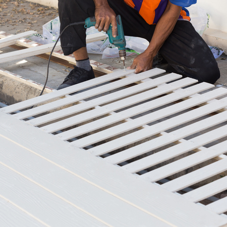carpenter hands using electric drill on wood at construction siteの写真素材