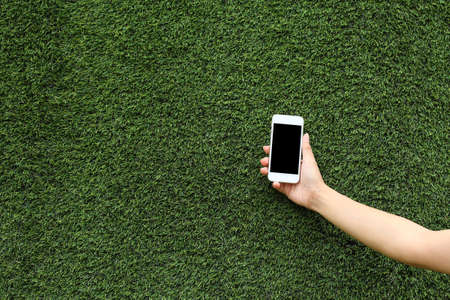 hand holding mobile phone with green grass backgroundの写真素材