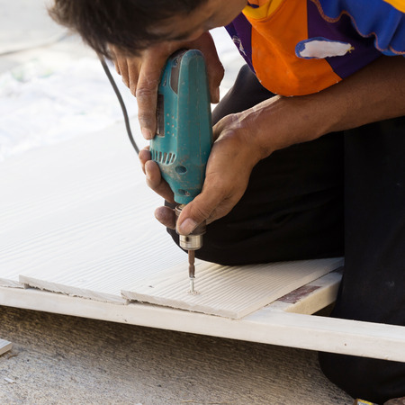 carpenter hands using electric drill on wood at construction siteの写真素材