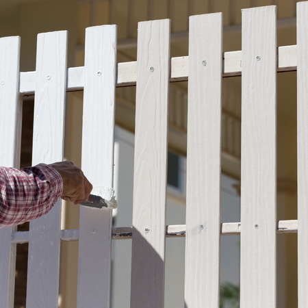 hand worker holding brush painting white on wood fenceの写真素材