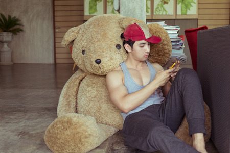 lifestyle of man using a mobile phone in home with big fluffy doll bearの写真素材