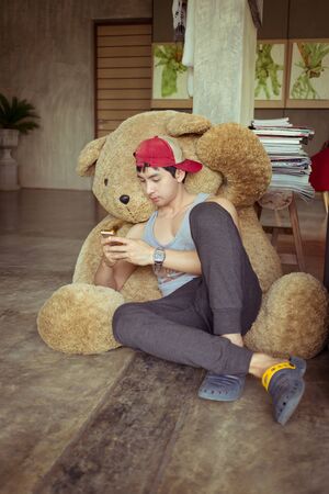lifestyle of man using a mobile phone in home with big fluffy doll bearの写真素材