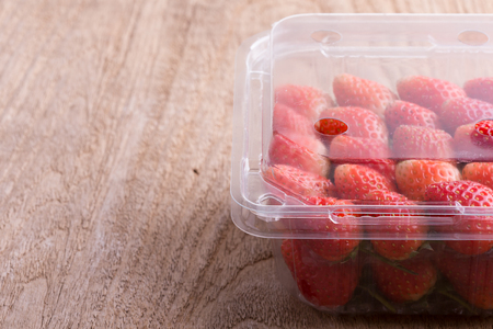 red ripe strawberry in plastic box of packaging on wood tableの写真素材