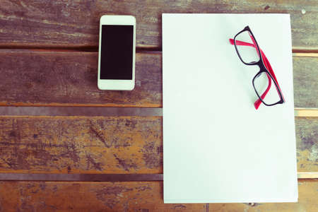top view of creative workspace with white paper blank and mobile phone on wood tableの写真素材
