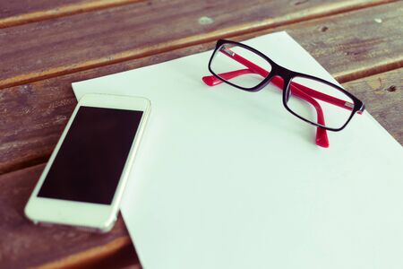 top view of creative workspace with white paper blank and mobile phone on wood table