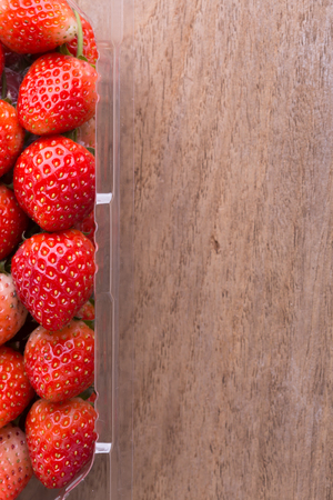 red ripe strawberry in plastic box of packaging on wood tableの写真素材