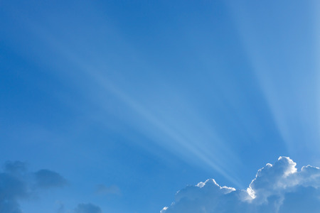 light rays of sun beam through clouds in clear blue sky background