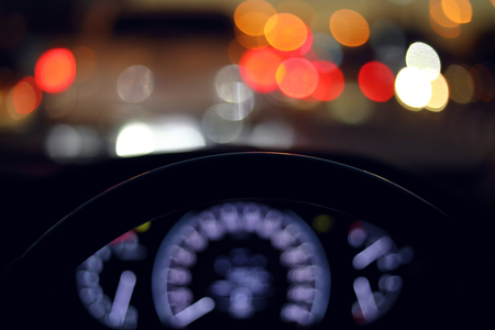 drive vehicle car travel road trip at city night with traffic light on street, image focus steering wheel and blur bokeh abstract backgroundの写真素材
