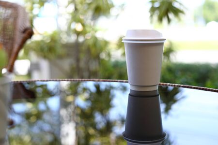 take away cup for hot coffee drink put on glass table inside garden cafe in the morning dayの写真素材