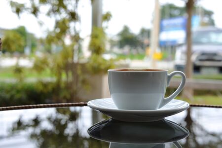 white cup of hot coffee drink put on glass table in cafe with natural park view backgroundの写真素材