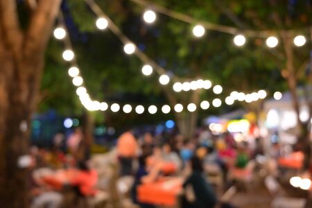 people crowd in night party festival of outdoor garden with light bulb hanging decoration, image blur used for celebration backgroundの写真素材