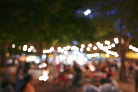 people crowd in night party festival of outdoor garden with light bulb hanging decoration, image blur used for celebration backgroundの写真素材