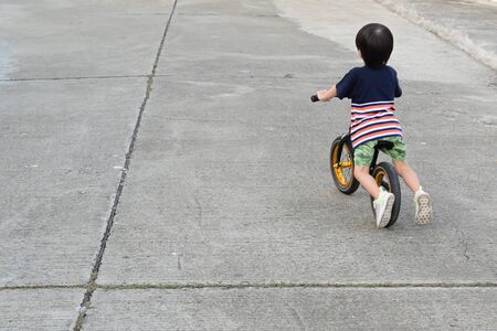 cute boy riding balance bike on streetの写真素材