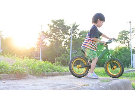 cute boy playing balance bike in the park with sun light in the morning dayの写真素材