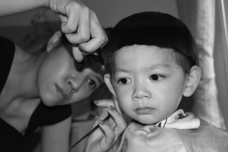 mother hairdresser using scissor haircut a cute baby boy in home barberの写真素材