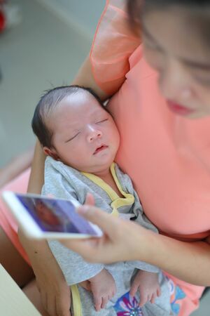 mother playing mobile phone in business home office with cute baby newborn sleeping