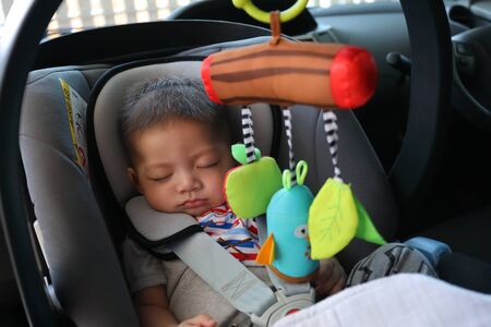 cute baby boy sleeping in car seat safety belt lock protection drive road tripの写真素材