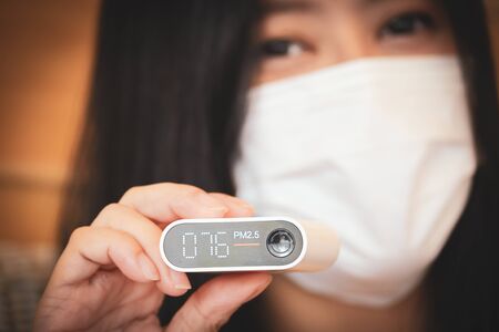 asian woman wearing face mask and using automatic measuring of air dust pollution pm2.5 with unhealthyの写真素材