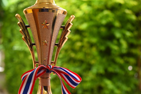 beautiful golden trophy with ribbon on green tree backgroundの写真素材