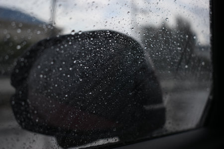 side mirror of car on road in raining day, abstract blur background