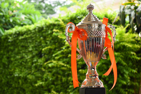 beautiful golden trophy with orange ribbon on green tree backgroundの写真素材