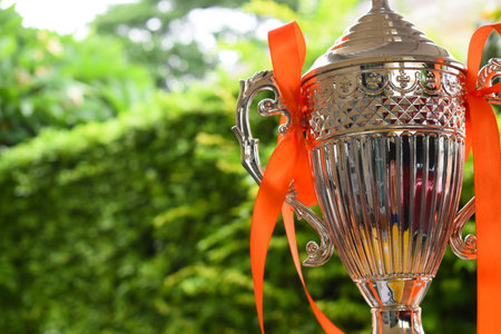 beautiful golden trophy with orange ribbon on green tree backgroundの写真素材
