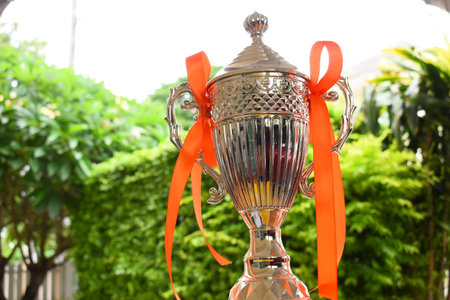 beautiful golden trophy with orange ribbon on green tree backgroundの写真素材