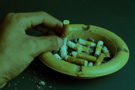Hand extinguishing cigarette, cigarette butt in ashtray, dark green backgroundの写真素材
