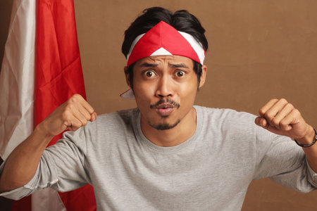 young man celebrating Indonesia's independence victory with a bunch of cloth on his head and excited...