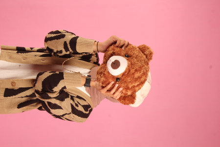 beautiful young woman standing carrying stuffed monkey with closed face, pink background