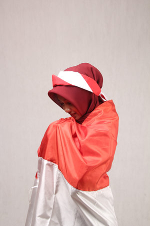 portrait of a woman wearing an Asian hijab kissing the red and white flag cloth as a shawl on her body, the concept of Indonesian independenceの写真素材