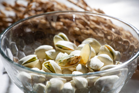 closeup Pistachio nuts in white glass bowl isolated on white background with blurred wheat stalks