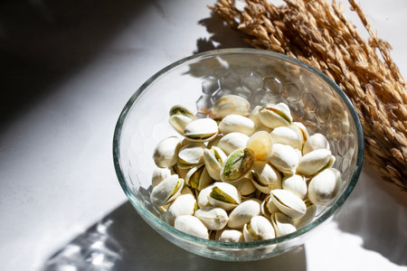 pistachio nuts, cashew nuts, fried nuts in white glass bowl isolated on light shadow background, negative space, top viewの写真素材