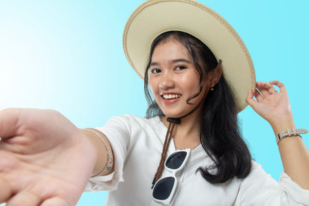 Fashion portrait of young Asian traveler woman wearing straw hat and hands facing forward, isolated...