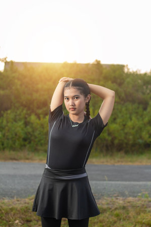 portrait of beautiful Asian sports girl in black sportswear standing shining her shoulders in the...