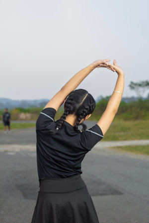 Beautiful Asian girl standing with her back to the camera doing body and arm warm-up movements for...