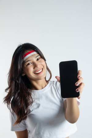 an enthusiastic girl wearing a headband shows to a black screen cell phone, concept of indonesian independenceの写真素材