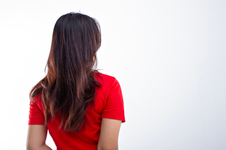 Rear view of a woman with black and brown hair in a stylish red t-shirt with her back facing the camera isolated on a white background, women's hair advertisementの写真素材