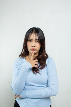 Looking gloomy and emotional with her hand on her chin, a beautiful girl with a blue casual top and long hair, the woman stands with a movement of her handの写真素材