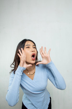 Asian woman talking loudly with hand gestures on her cheeks, the woman is wearing a blue casual topの写真素材