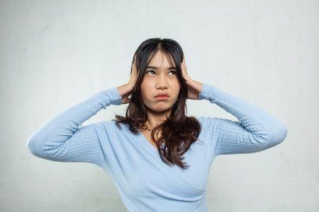 Beautiful Asian woman holding headache or dizziness on white background, the woman is wearing blue top casual suit, dizziness problem, work dizziness, health stress advertisingの写真素材