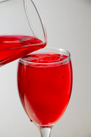 close-up of two red liquid glasses filled with red liquid being poured over them.