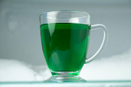 glass cup with green liquid inside. frozen ice snow background in freezerの写真素材