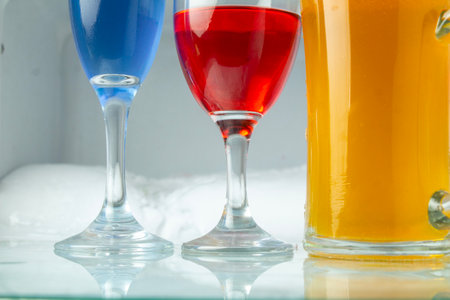Colorful cocktails in glasses, on glass table base and ice cooler background