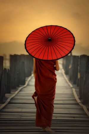 Myanmar Novice monk and holding  red umbrella walking on the U - Bein bridge Mandalay Burma.の写真素材