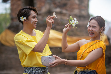 A beautiful Young Thai couple wearing Thai costumes playing in the water during Songkran in the templeの写真素材