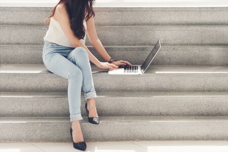 Working women white shirt blue jean clothe black long hair use computer laptop sitting on stairの写真素材